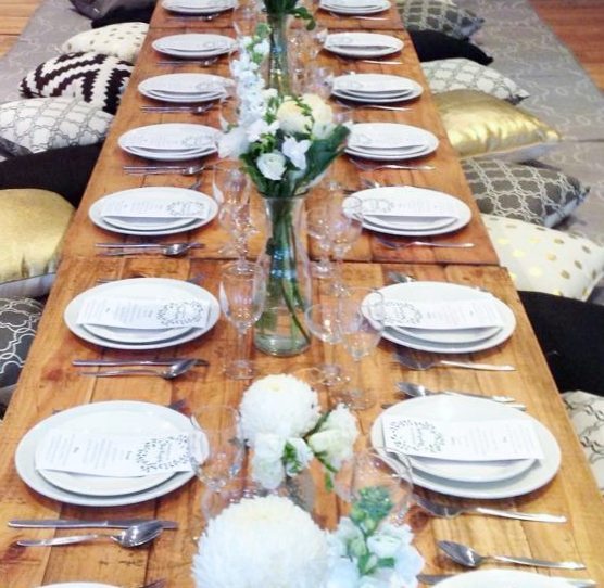 Reclaimed trestle tables on low boho legs with plates and cutlery. Cushions are around the sides of the table