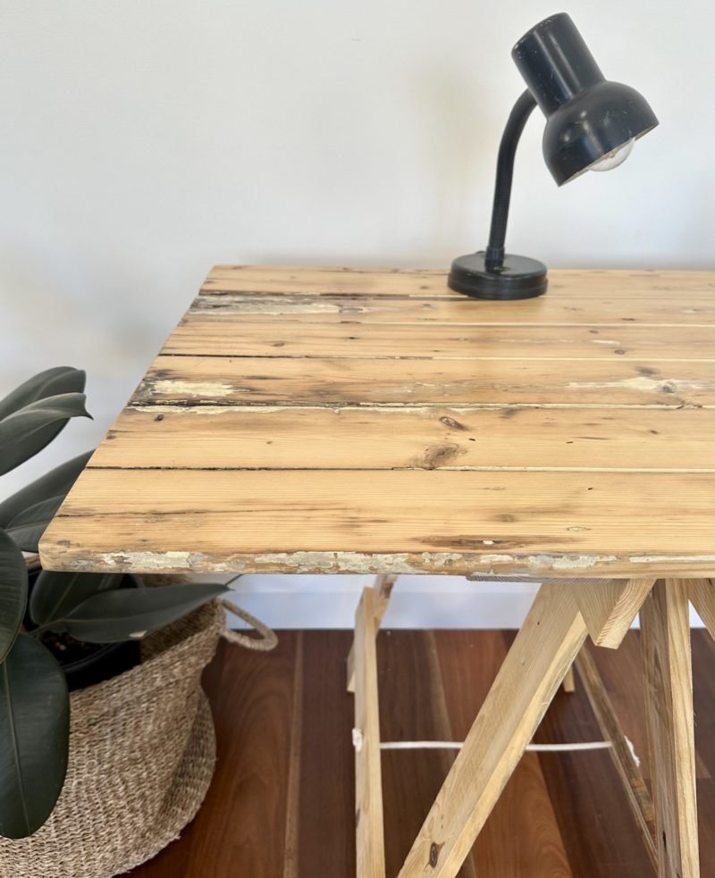The end of a light reclaimed farmhouse door trestle table with a table lamp on top and sitting upon a reclaimed pine trestle leg