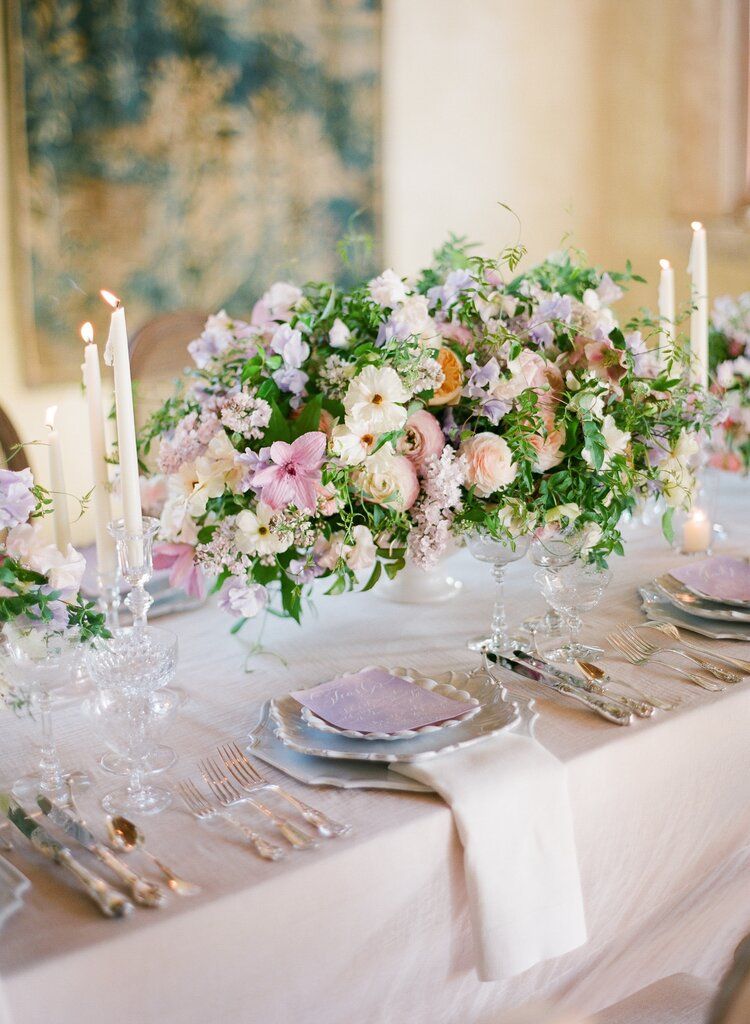 Tables with white table cloths and a large boquet of flowers in the centre with plates and cutlery for guests